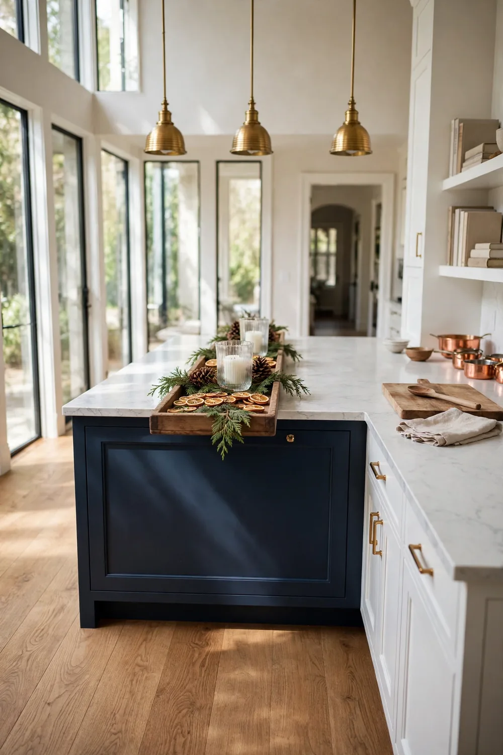 Long wooden tray with pinecones, dried oranges, cedar sprigs, and flameless candles centered on a navy kitchen island