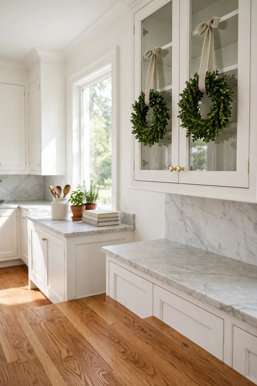 Small boxwood wreaths tied with ribbon hanging on the doors of white upper kitchen cabinets